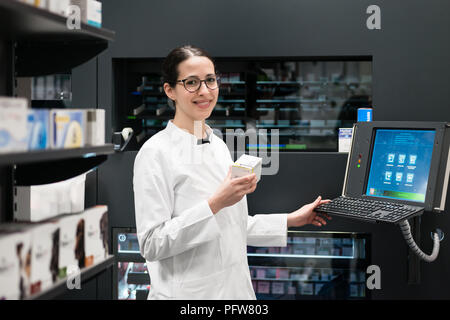 Pharmacien à l'aide d'un ordinateur tout en gérant le stock de médicaments dans la pharmacie Banque D'Images