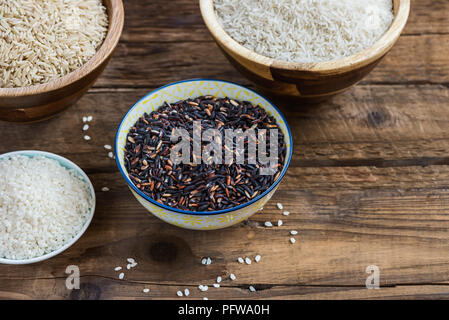 Différents types de riz dans des bols en bois comme le basmati, brun et noir sur fond gris Banque D'Images