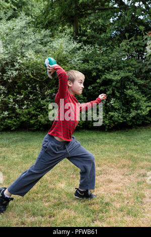 10 ans garçon en train de lancer un ballon de football sur sa pelouse Banque D'Images