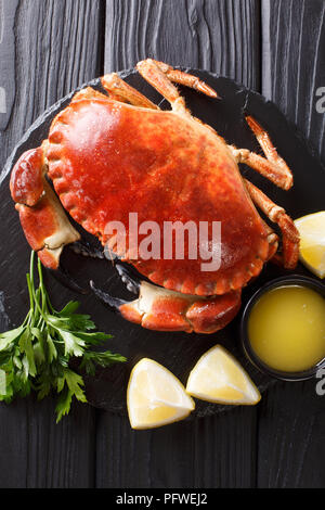 Menu de fruits de mer : délicatesse bouilli crabe brun avec la sauce, le persil et citron sur une liste de sélection gros plan sur une table en bois noir. Haut Vertical Vue de dessus Banque D'Images