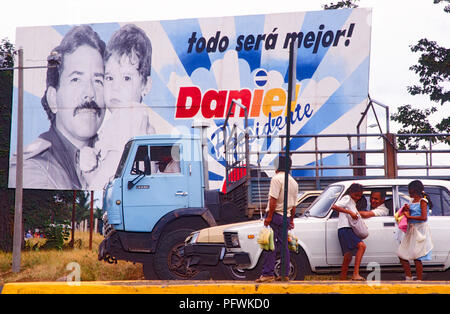 Managua, Nicaragua, élections, Feb 1990;adolescents vente de fruits, de tissus, de chemises et d'autres biens aux conducteurs à un carrefour avec Ortega affiche électorale derrière. Banque D'Images