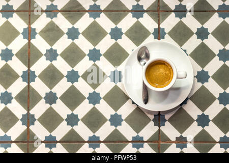 Une tasse de café espresso sur une plaque avec une cuillère placée sur un vieux plancher de carreaux de céramique. Banque D'Images