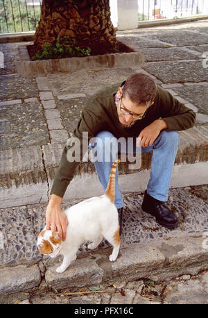 L'homme de caresser un chat tabby et blanc dans la rue. Banque D'Images