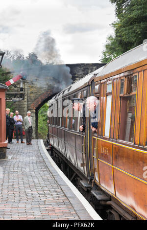 Severn Valley Railway steam train attend à vintage UK gare Arley, soufflant de la fumée comme garde & passager stick leurs têtes hors de la fenêtre transport. Banque D'Images