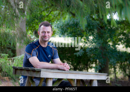 Beau homme en été T-shirt assis à l'extérieur isolé dans le pays pub bière jardin, Royaume-Uni, conscient des règles de distanciation sociale, en attente de boire. Banque D'Images
