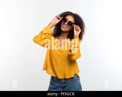 Belle african american woman with afro hair en jaune et usure sunglasses smiling to camera sur mur blanc arrière-plan. Cute girl's por Banque D'Images