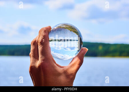 Main tenant une bille de verre reflétant le lac et la forêt. Notion d'environnement, de la protection de la nature, l'écologie. Selective focus Banque D'Images