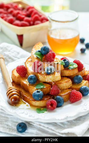 Un petit-déjeuner traditionnel - French toast avec du miel et de baies fraîches - les framboises et les bleuets dans une assiette blanche sur la table. Style rustique. Selective Banque D'Images