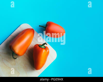 Le poivre dans haut Voir Photo modèle avec copie espace trois gros poivrons rouges sont situées sur une planche à découper sur un fond bleu Banque D'Images