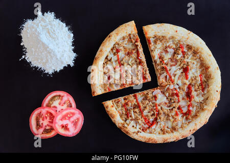 Thon au four pizza, tas de farine et de tranches de tomate sur fond noir Banque D'Images
