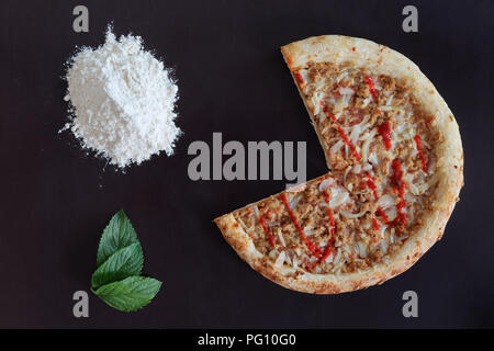 Pizza tronquée, tas de farine et de feuilles vertes sur fond noir Banque D'Images
