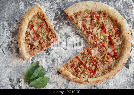 Tranches de pizza au thon et de feuilles vertes sur fond sombre parsemée de farine blanche Banque D'Images Tranches de pizza au thon et de feuilles vertes sur fond sombre parsemée de farine blanche Banque D'Images