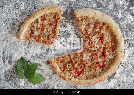 Tranches de pizza au thon et de feuilles vertes sur fond sombre parsemée de farine blanche Banque D'Images Tranches de pizza au thon et de feuilles vertes sur fond sombre parsemée de farine blanche Banque D'Images