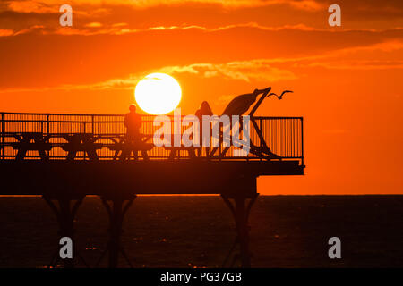 Pays de Galles Aberystwyth UK, jeudi 23 août 2018 UK Weather : un magnifique coucher de soleil sur les gens qui se profile sur la jetée de Aberystwyth, sur la côte ouest de la Baie de Cardigan au Pays de Galles, à la fin d'une journée de blustery cool vents violents et de fortes averses de pluie.La météo pour le week-end férié d'août devrait être très en suspens, avec de fortes pluies susceptibles pour de nombreux domaines Photo © Keith Morris / Alamy Live News Banque D'Images