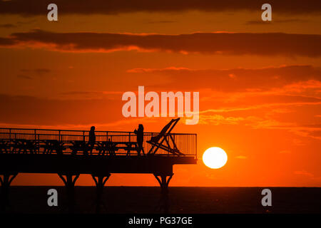 Pays de Galles Aberystwyth UK, jeudi 23 août 2018 UK Weather : un magnifique coucher de soleil sur les gens qui se profile sur la jetée de Aberystwyth, sur la côte ouest de la Baie de Cardigan au Pays de Galles, à la fin d'une journée de blustery cool vents violents et de fortes averses de pluie.La météo pour le week-end férié d'août devrait être très en suspens, avec de fortes pluies susceptibles pour de nombreux domaines Photo © Keith Morris / Alamy Live News Banque D'Images