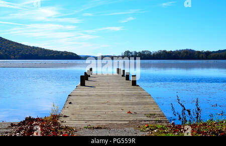 Quai de bois s'étendant sur l'eau du lac. Belle image sereine de jetée en bois avec les eaux bleu et bleu ciel, les collines au loin en arrière-plan. Banque D'Images