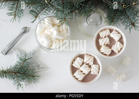 Dans marshmelow avec cacao tasses blanc et les guimauves dans un bocal en verre sur un tableau blanc avec des branches d'épinette, une guirlande et une étoile blanche. Selective focus Banque D'Images