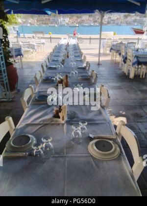 Grèce, la belle île de Poros, près d'Athènes. Tables dans une rangée pour le dîner, tôt dans la soirée dans une taverne traditionnelle. Banque D'Images