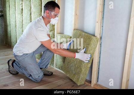 Travailleur dans des lunettes et un masque respiratoire l'isolation isolation laine de roche dans le cadre en bois pour les murs de maison pour barrière froide. Chaud confortable Banque D'Images