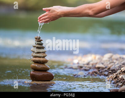 Close-up résumé image de femme part verser de l'eau sur les différentes tailles inégales brun naturel et la forme des pierres comme équilibrée pile pyramide monument Banque D'Images