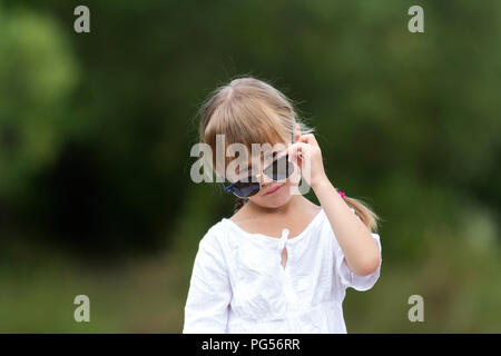 Portrait of cute assez drôle cool à la mode jeune fille en colère insatisfaite moody blonde avec tresses en robe blanche et des lunettes sur floue summ Banque D'Images