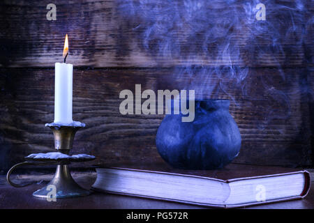 Witch pot sur livre de magie et de bougie allumée en chandelier brûle. Noir de fumée s'échappe du pot. Vieux bois sombre et l'arrière-plan. Halloween Banque D'Images