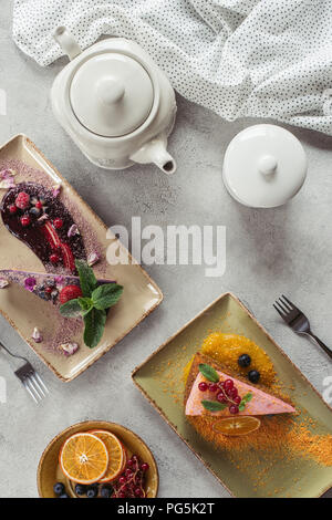 Mise à plat avec de doux gâteau aux carottes avec berry le remplissage, blueberry cake servi avec des feuilles de menthe et de pétales de violette, théière et le linge sur la table gris Banque D'Images