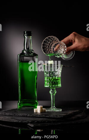 Cropped shot of woman pouring absinthe en verre et sur cube de sucre sur fond sombre Banque D'Images