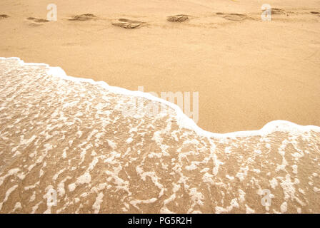 Empreintes laissées sur le bord de la mer et à la ligne d'écume formée par les vagues se brisant sur une plage, copy space Banque D'Images
