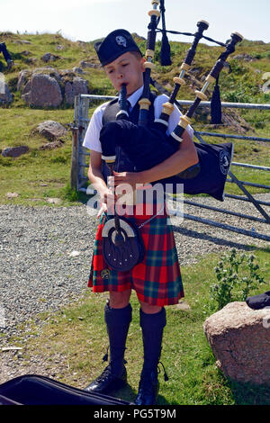 Jeune garçon en robe Highland jouant la cornemuse et divertir les visiteurs de Fionnphort sur l'île de Mull Banque D'Images