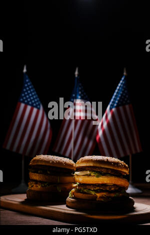 Hamburgers savoureux sur planche à découper en bois en face de petits drapeaux des États-Unis Banque D'Images