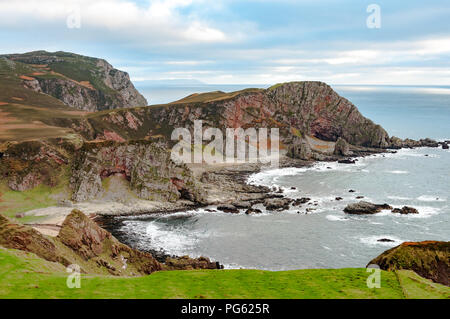 Une côte rocheuse avec des falaises de roche rouge et l'herbe au premier plan Banque D'Images