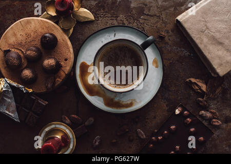 Portrait de tasse de café, les truffes sur tranche de bois, des bougies, des fèves de cacao, livres et deux barres de chocolat sur la table rustique Banque D'Images