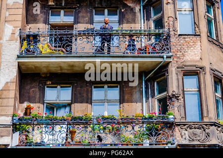 Un homme à la recherche vers le bas d'un balcon d'un immeuble délabré avec plâtre manquant à Poznań, Pologne (Poznan) Banque D'Images