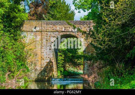 Un pont de pierre sur un ruisseau et un déversoir à Jesmond Dene, Newcastle, Angleterre, Royaume-Uni Banque D'Images