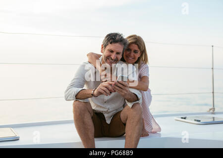 Mature couple looking at smartphone, assis sur un bateau à voile Banque D'Images