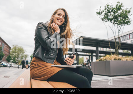 Jeune femme avec un ordinateur portable et un téléphone cellulaire dans la ville Banque D'Images