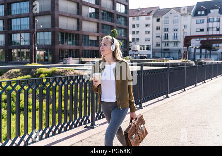 Jeune femme marche sur pont, boire du café, d'écouter de la musique avec des écouteurs Banque D'Images