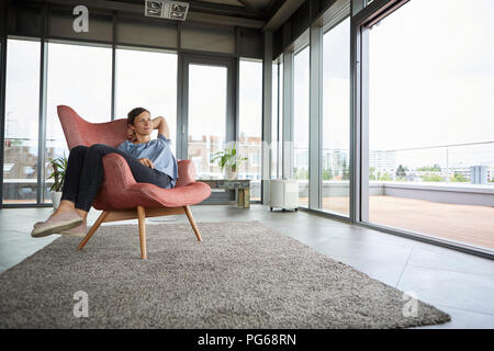 Femme assise dans un fauteuil relaxant à la maison Banque D'Images