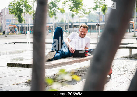 Smiling man lying on bench using tablet Banque D'Images