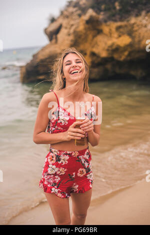 Portrait of happy young woman standing avec une bière sur la plage Banque D'Images