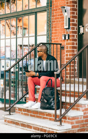 USA, NYC, Brooklyn, en attente de l'homme dans les escaliers, using smartphone Banque D'Images