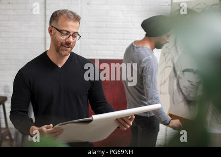 Smiling man looking at sketchbook dans un studio d'artiste Banque D'Images