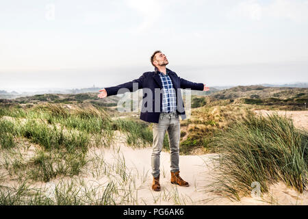 Homme debout dans des dunes avec les bras tendus Banque D'Images