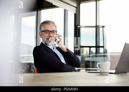 Woman on cell pohone at desk in office Banque D'Images