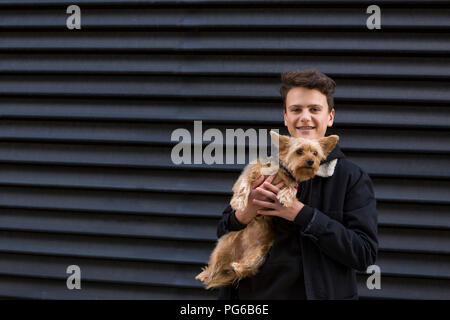 Portrait of smiling teenage boy avec son chien sur fond noir Banque D'Images