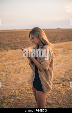 Young woman standing in field, using smartphone Banque D'Images