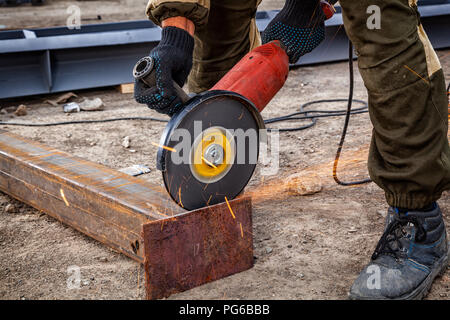 Portrait d'un jeune homme en uniforme brun Soudeur Soudeurs, cuirs, grinder metal une meuleuse d'angle sur le site de construction, orange étincelles voler à th Banque D'Images