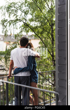 Vue arrière du couple dans des chemises de nuit debout sur balcon hugging Banque D'Images