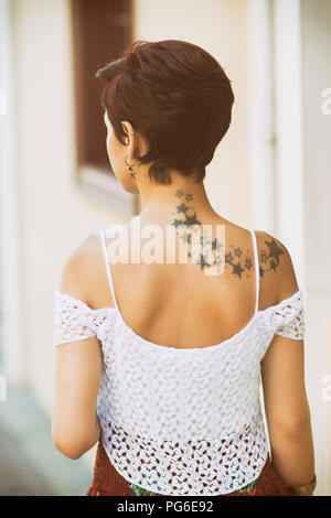 Vue arrière d'une jeune femme aux courts cheveux roux et des étoiles sur le dos tatouage standing outdoors Banque D'Images